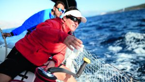 Women in sailing: A woman wearing a red jacket, sunglasses and a sun visa preparing to use a winch