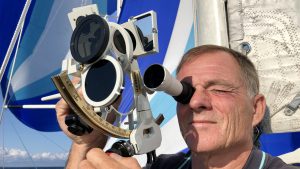 A man using a sextant to navigate on the deck of a boat