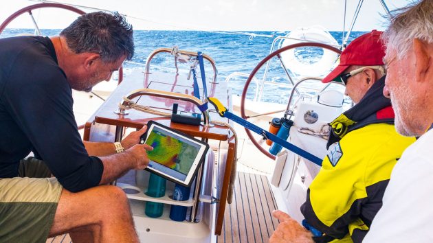 Sailors on the deck of a boat looking an an ipad with weather information on it