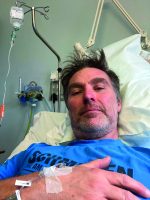 A man wearing a blue t shirt in hospital hooked up to an IV due to carbon monoxide poisoning