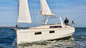 A man standing up wearing a black lifejacket helming a Beneteau Oceanis 35.1