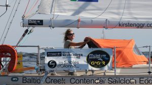 Kirsten Neuschafer wearing sunglasses while helming her boat which has a white hull