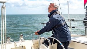 Guy Waites, a sailor, pulling on a line on a yacht while wearing a blue coat