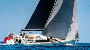 A woman with blonde hair in a pony tail and wearing a white tshirt at the helm of an Oyster 495