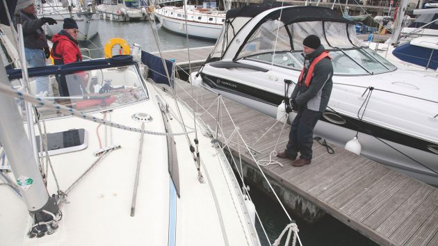 A person wearing a lifejacket and bobble hat on the pontoon holding a rope while the skipper tries to berth in a gale