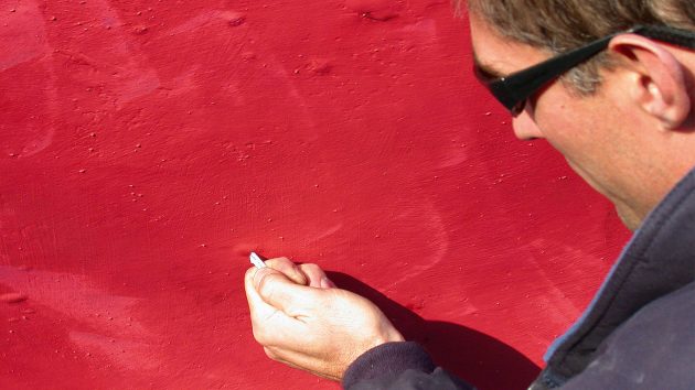 A man is draining hull moisture out of a blister. He is wearing sunglasses.