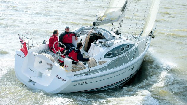 A small yacht with three people on it is gliding through fairly calm water.