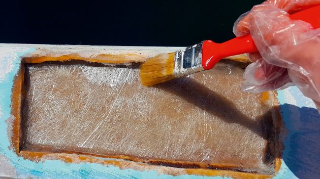 A close-up. of someone holding a small paintbrush and applyinh a paste to some plywood.