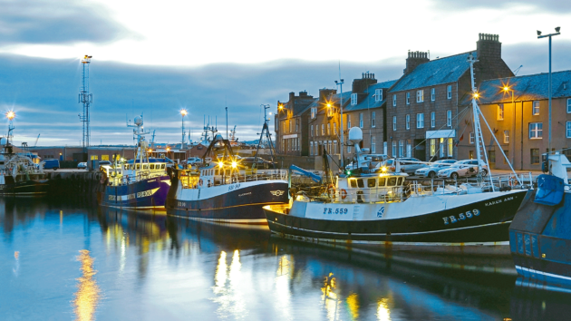 The fishing village of Peterhead lit up in the evening with fishing vessels moored up