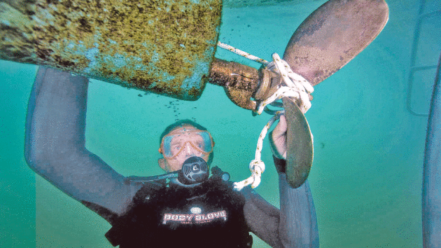 Someone in diving gear underwater next to a propeller