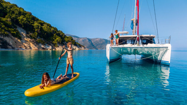 A catamaran in the water with two kids on a paddleboard