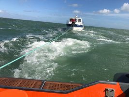 A broken down cabin cruiser boat is towed by a lifeboat