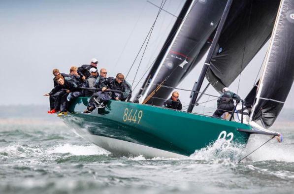 Men sitting on the edge of a green racing boat with black sails