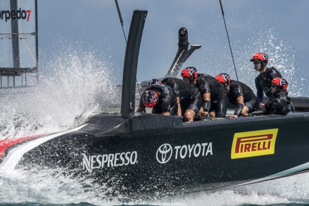 Dressed in black and wearing red helmets, America's Cup sailors pedal on board