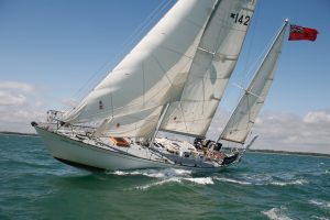 A yacht with white sails flying an ensign cruises