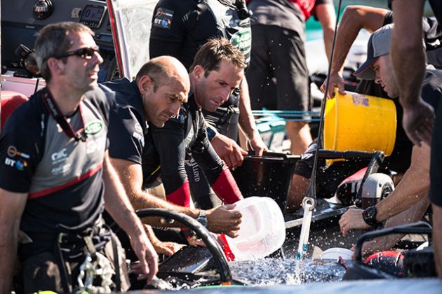 Members of Land Rover BAR dressed in red and black use buckets to bail out a boat