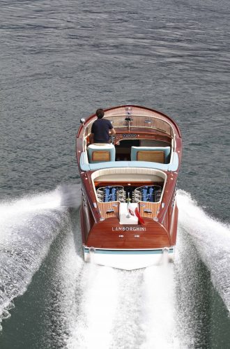 A wooden Riva motorboat speeds across a river in Italy