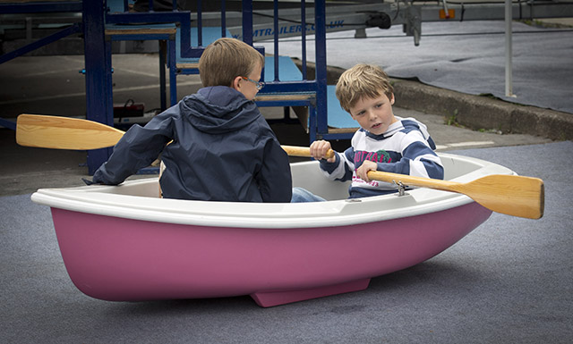 Two children pretend to row in a pink rowing boat