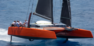 A red catamaran with black sails foiling on the water