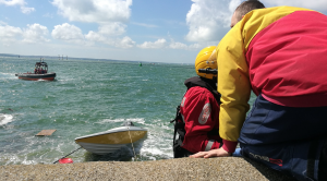 A speedboat on the rocks with two men in red and yellow jackets at Southsea