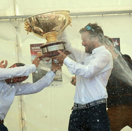 Champagne is sprayed over men as they hold a gold trophy