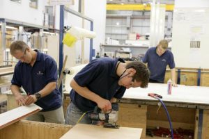 Three apprentices in t-shirts work with wood at Fairline Yachts