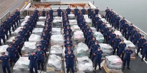 US Coast Guard officials in blue uniforms stand next to some of the cocaine seized from drug dealers in the Eastern Pacific Ocean