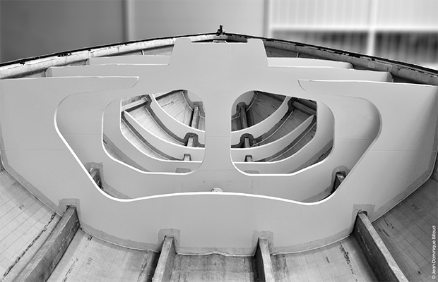 A black and white photo of the hull of a foiling boat under construction
