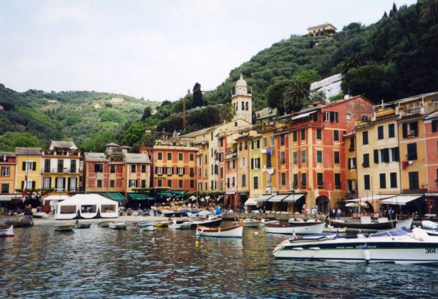 Yachts are moored next to brightly coloured houses in Italy