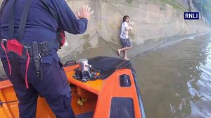 A man holding a dog is balancing on chains while awaiting rescue from the RNLI on London