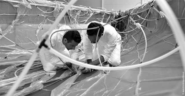 Two men in white suits work on the hull of the Figaro Bénéteau 3