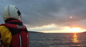 An RNLI volunteer wearing a white helmet and red lifejacket looks for missing dinghy sailors