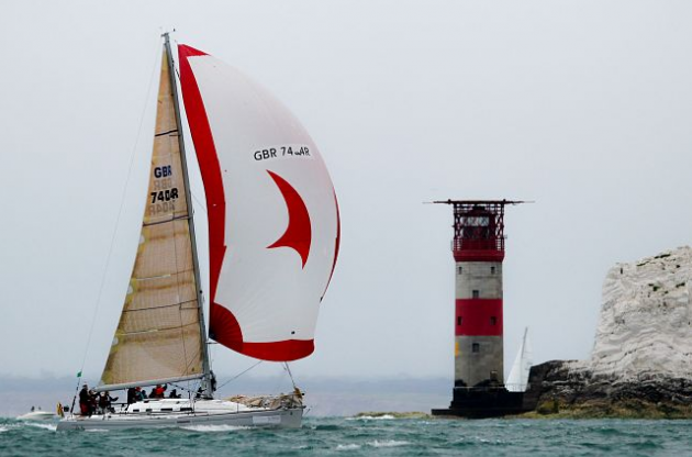 A racing yacht with a red and white sail passes the Needles and its iconic red and white lighthouse