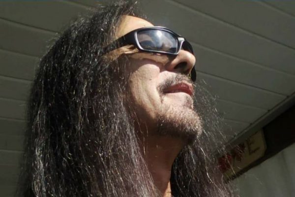 A man with long dark hair and wearing sunglasses