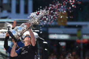 Peter Burling wearing his team colours lifts up the America's Cup