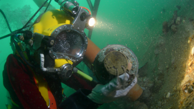 A diver wearing a full face mask with finds from a wreck