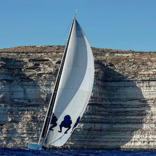 A yacht with white sails close to a cliff