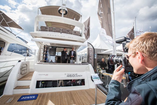 Two men on the aft of a motor yacht as a photographer takes a picture