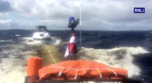 An RNLI orange all-weather lifeboat tows a motor cruiser in rough swells off Lough Ree