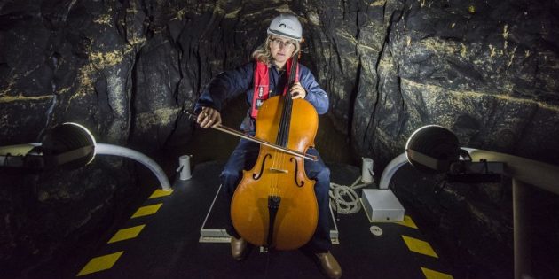 A woman wearing a hard hat playing a cello on a boat inside a tunnel