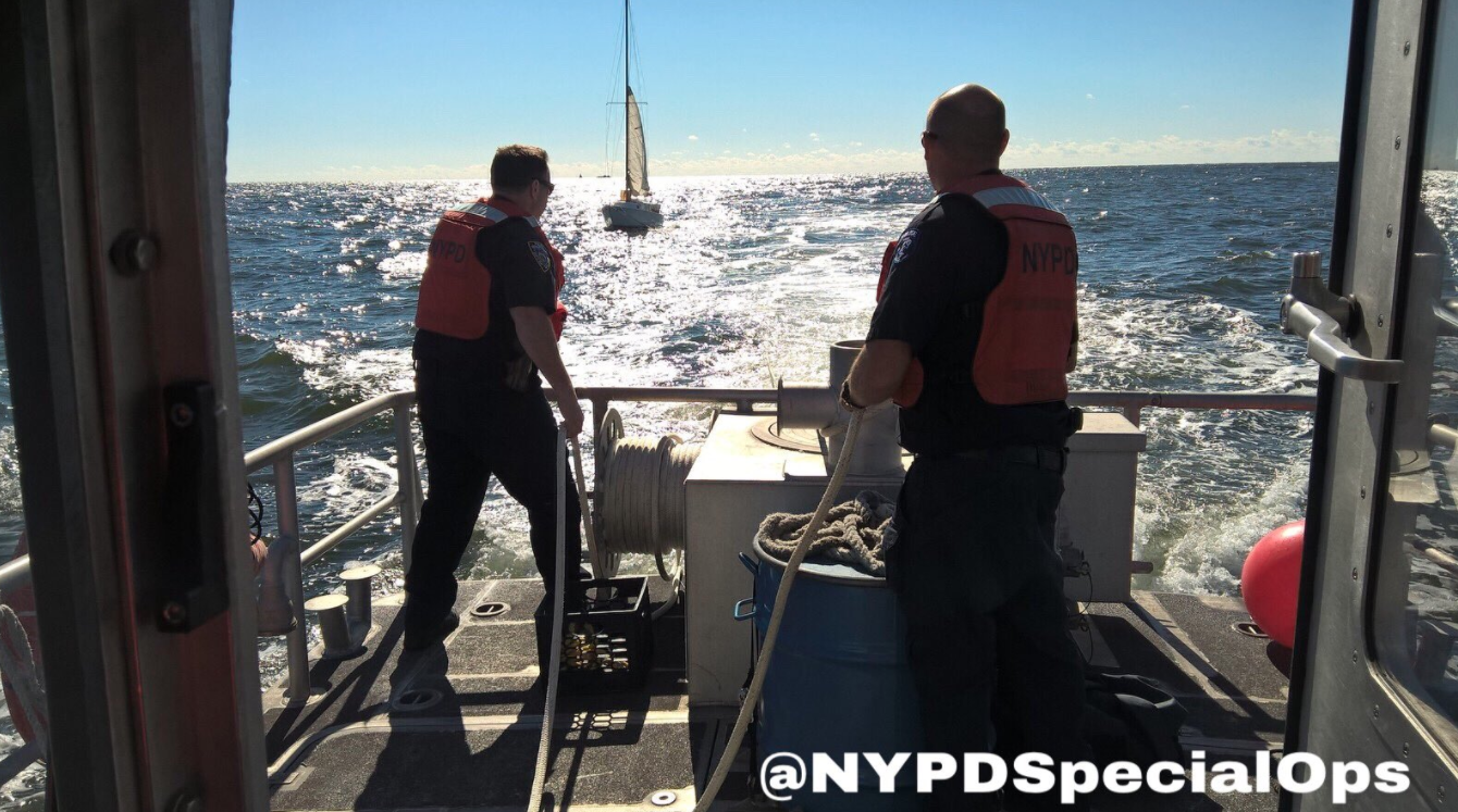 Two NYPD officers are the back of a boat towing a yacht