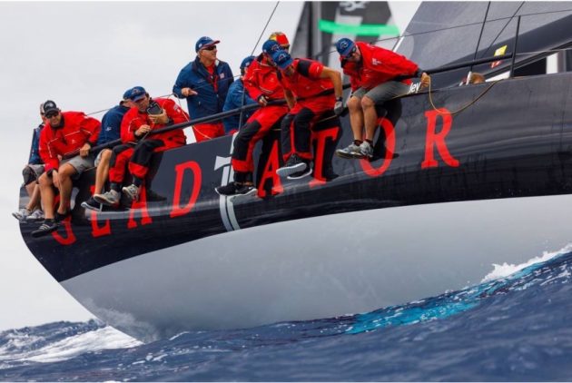 Sailors dressed in red sitting on the edge of a sailing superyacht