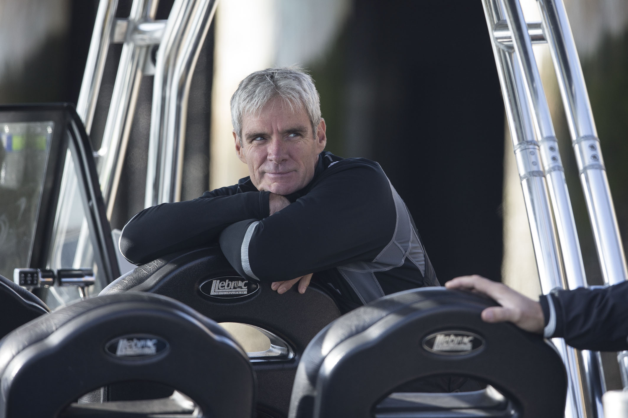 America's Cup sailor Grant Simmer wearing a black and grey top and leaning against a vehicle