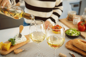 Woman pouring generic Sauvignon Blanc white wine into two glasses on a table with cheese and salad