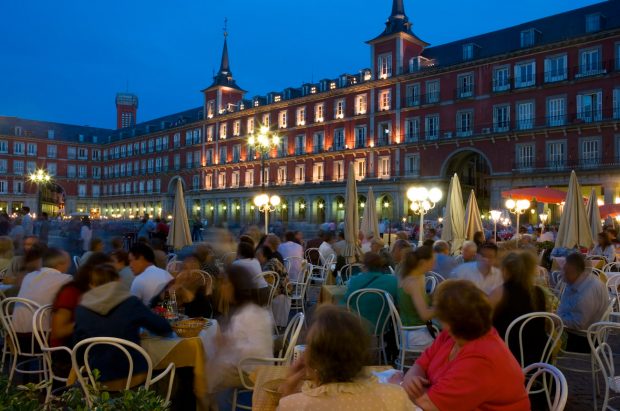 A city square in Madrid at dusk with people sitting at tables eating and drinking