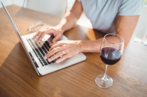 Glass of wine next to man using laptop