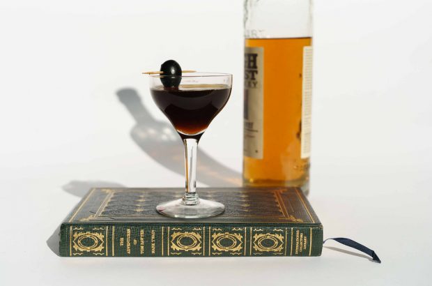 A cocktail sitting on a book next to a bottle of whiskey