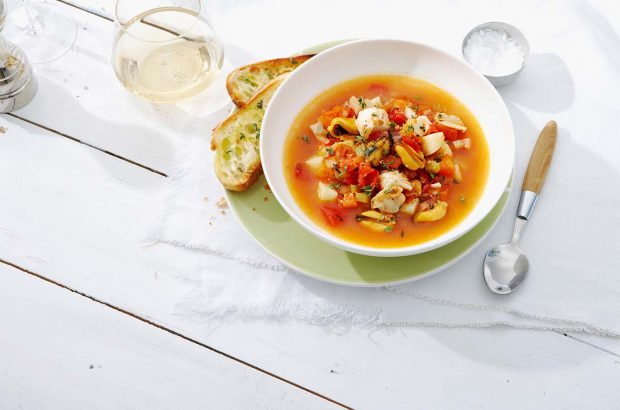 A bowl of bouillabaisse with bread and a glass of white wine