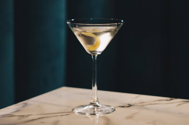 A Martini cocktail on a marble top in front of a dark blue curtain