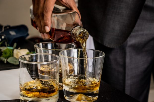 A hand pouring whisky into three glasses